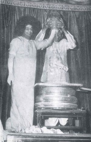 Swami kreuje wibhuti podczas Mahaśiwaratri w wazie trzymanej przez Kasturiego
    <br>(z książki <i>Loving God</i>)